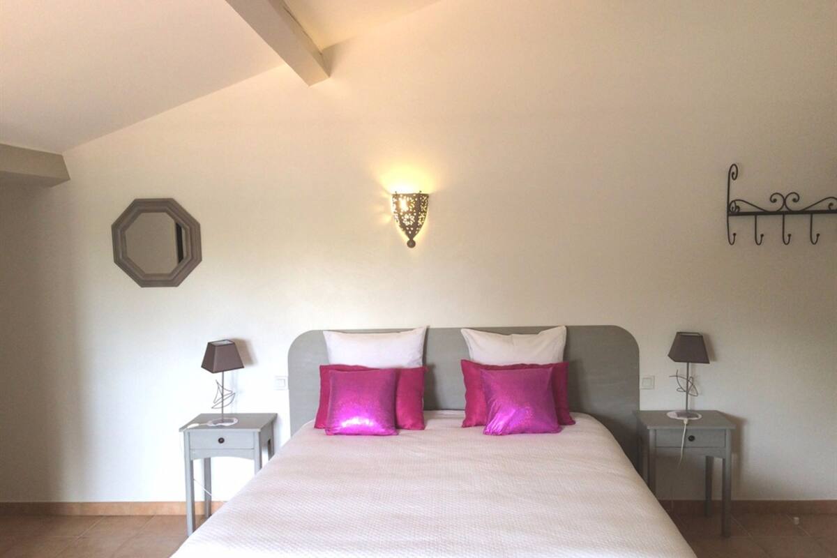 A bedroom with a bed, two nightstands, a wall-mounted light fixture, and a decorative wall piece.