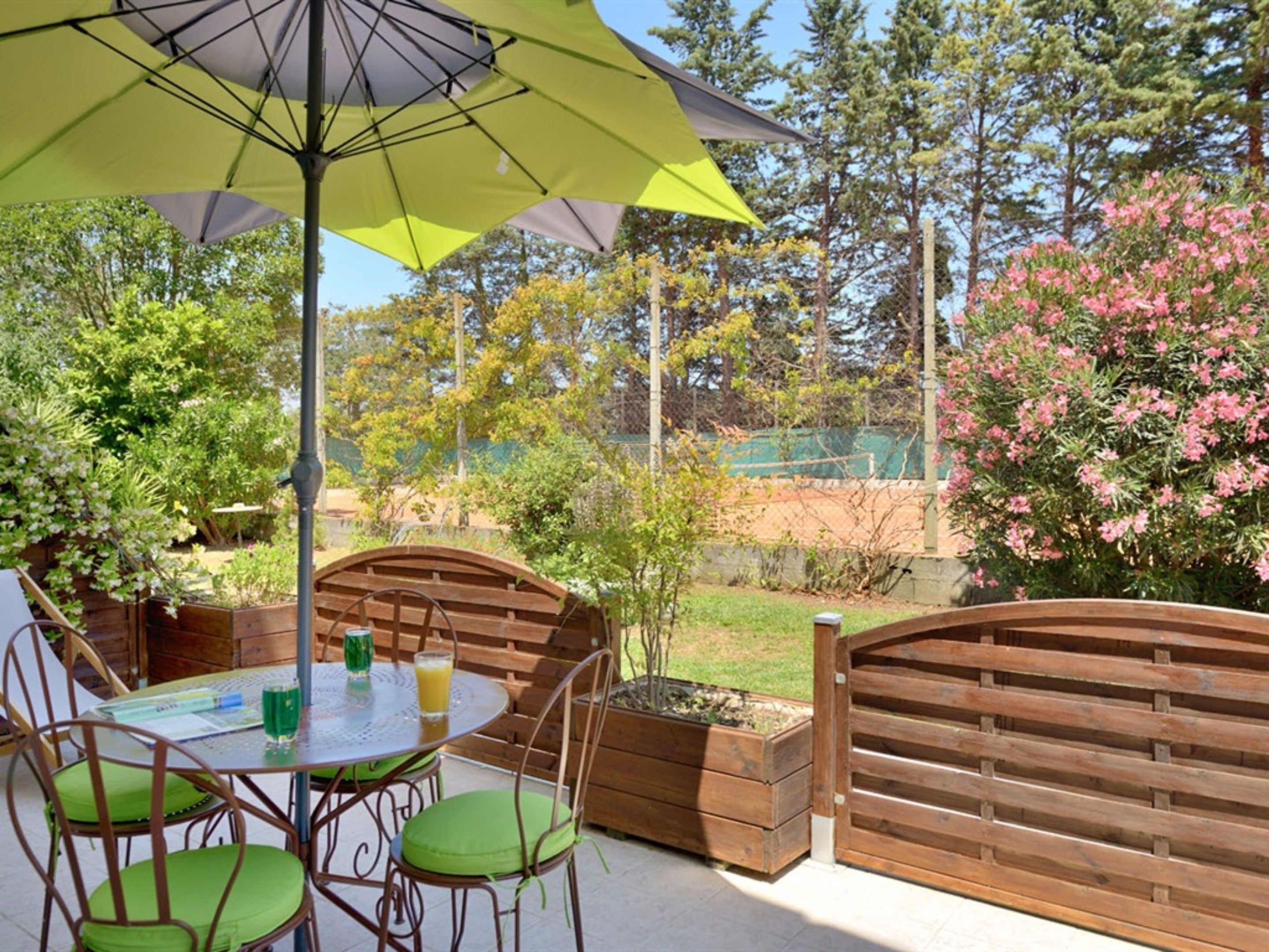 Une terrasse extérieure avec une table ronde, des chaises vertes et un grand parasol.