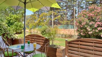Une terrasse extérieure avec une table ronde, des chaises vertes et un grand parasol.