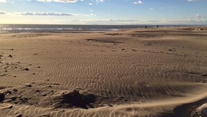 Ampia spiaggia sabbiosa con impronte e rocce, cielo sereno e vista sull'oceano in lontananza.