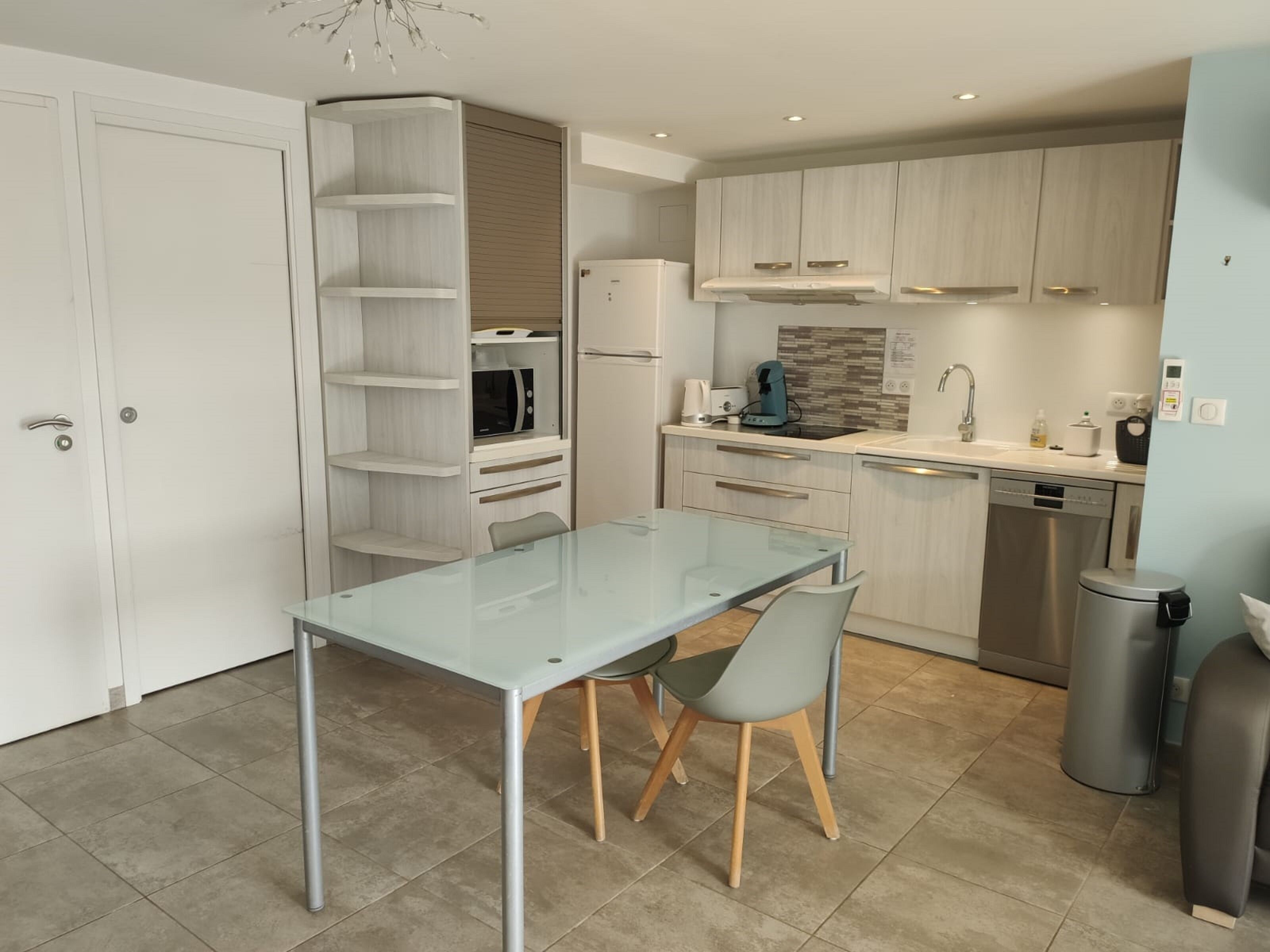 A modern kitchen with a glass dining table, built-in shelves, and contemporary appliances.