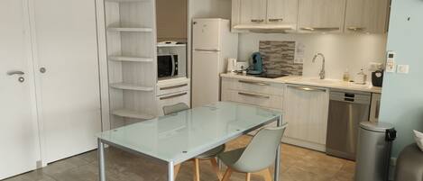 A modern kitchen with a glass dining table, built-in shelves, and contemporary appliances.