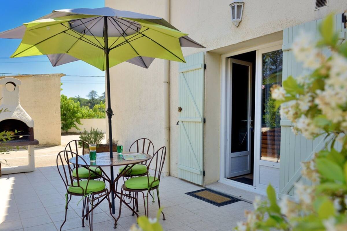 An outdoor patio with a table and chairs, a grill, and a door with shutters.