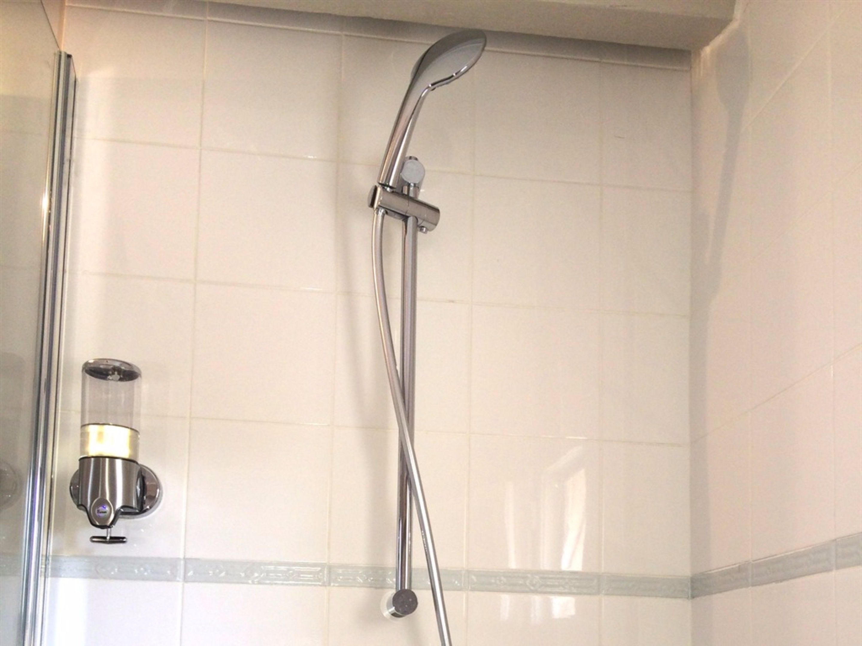 Une douche équipée d’un pommeau de douche à main et d’un robinet fixé au mur.