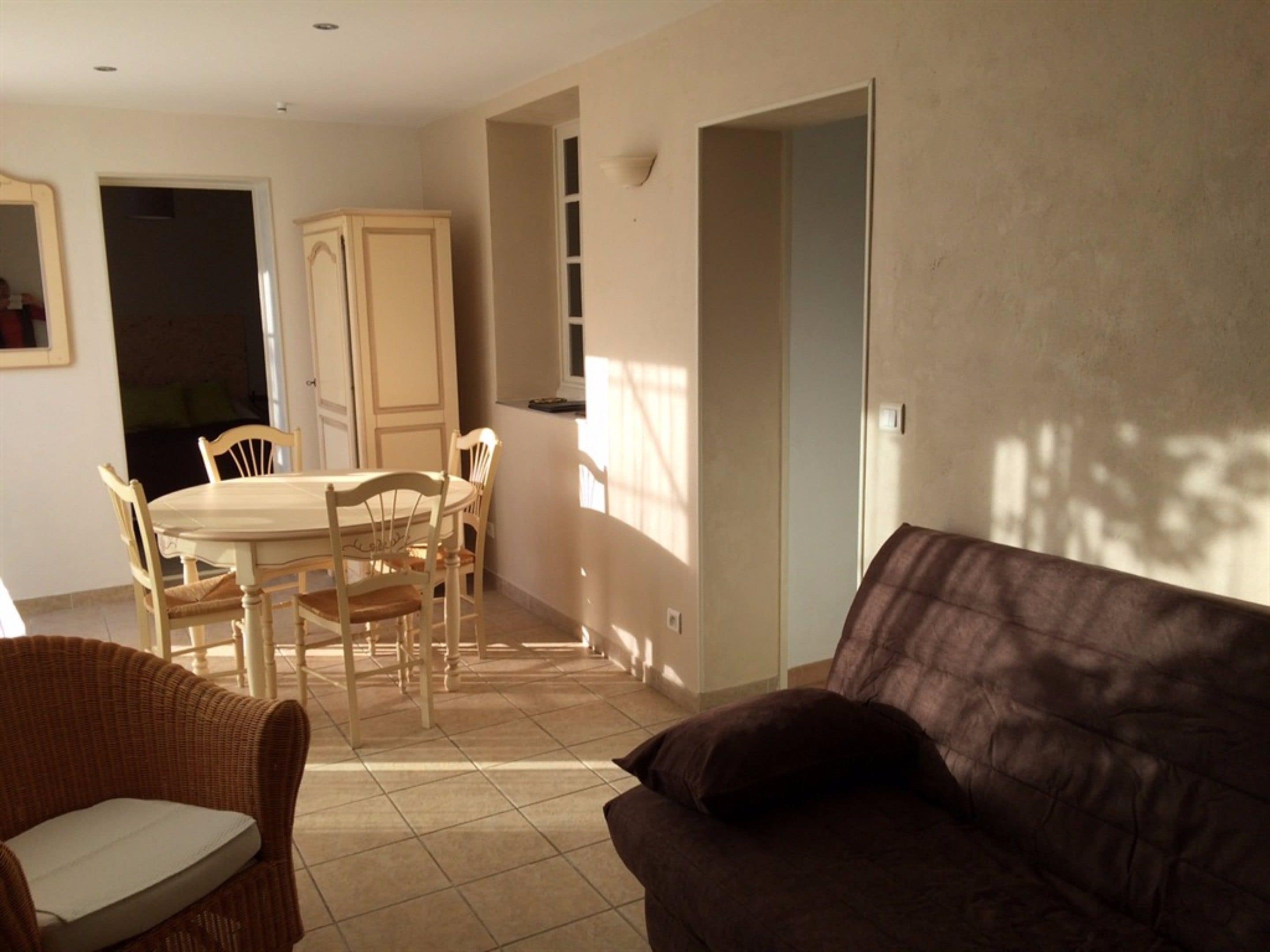 Un salon avec un canapé marron, une table à manger avec des chaises, et un coin cuisine à l’arrière-plan.