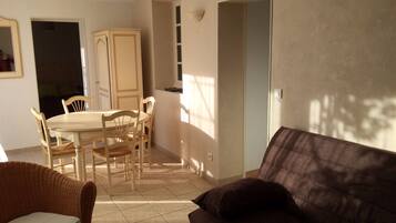 Ein Wohnzimmer mit braunem Sofa, einem Esstisch mit Stühlen und einer Küche im Hintergrund.