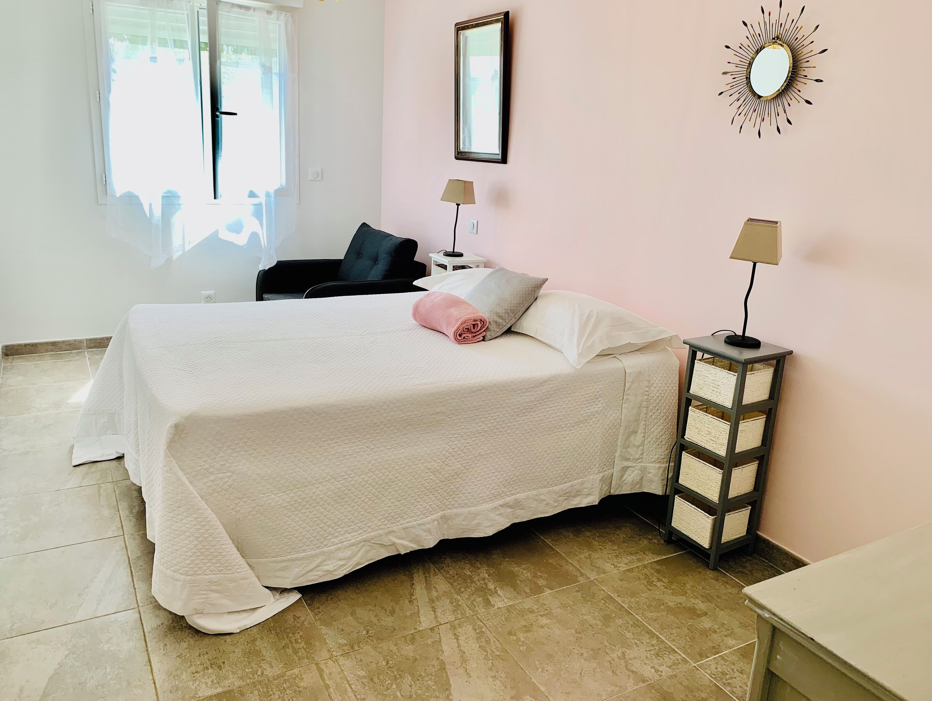 A neatly arranged bedroom with a bed, a chair, a nightstand, and a lamp.