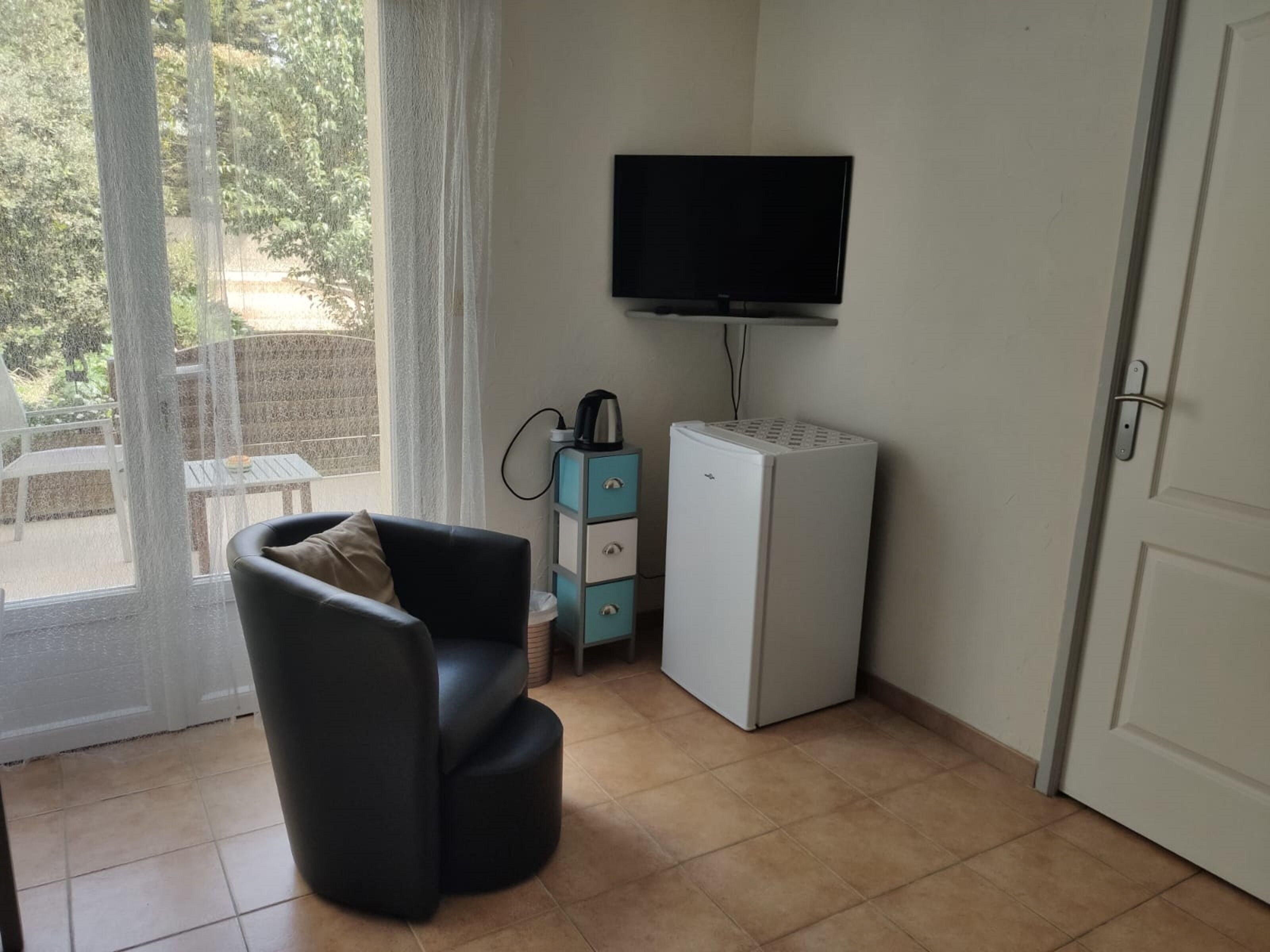 A room with a black chair, a small white refrigerator, a television mounted on the wall, and a door.