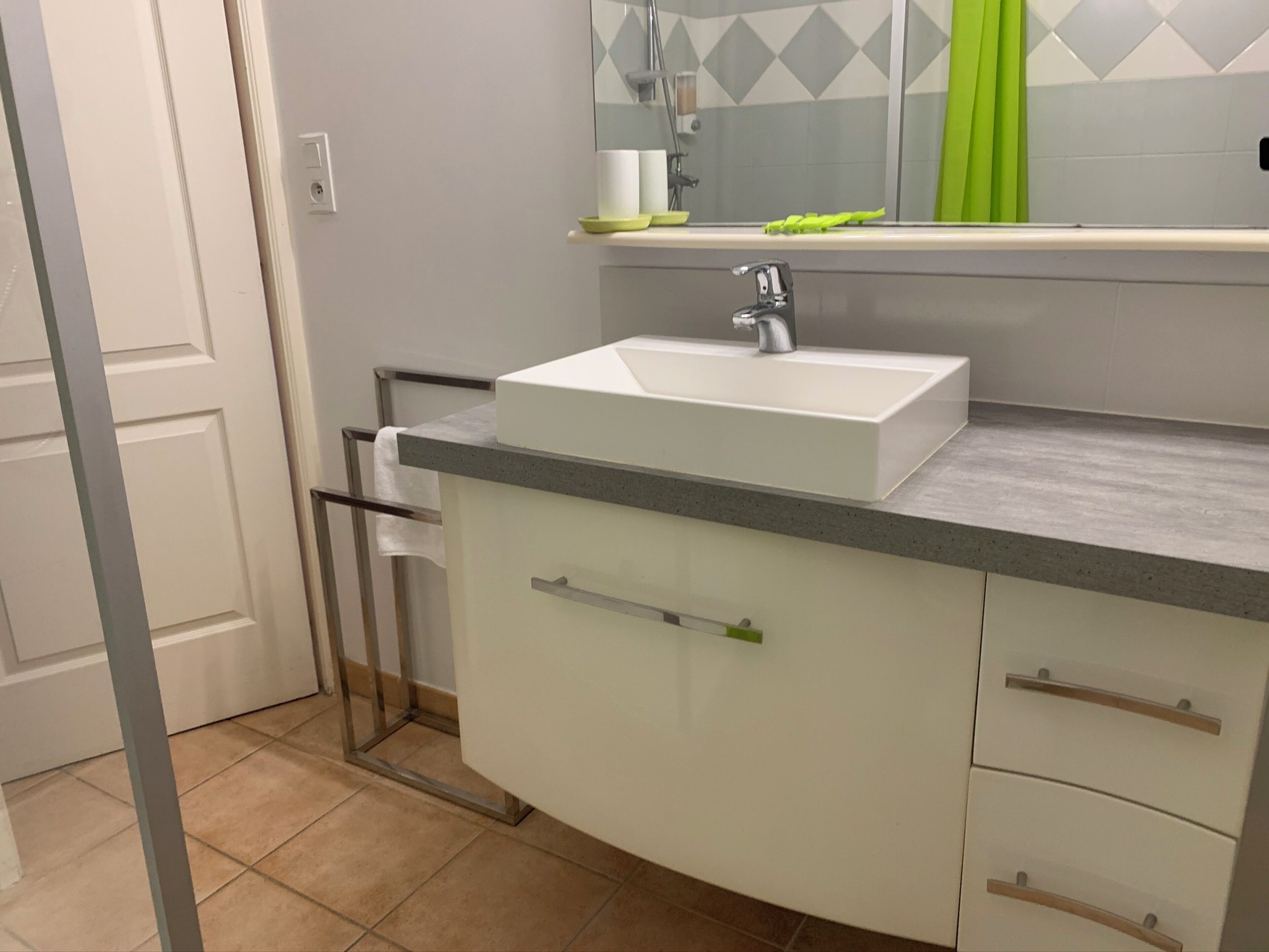 Une salle de bain avec un lavabo blanc, un miroir et un rideau de douche vert.