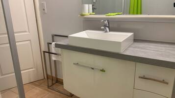 Une salle de bain avec un lavabo blanc, un miroir et un rideau de douche vert.
