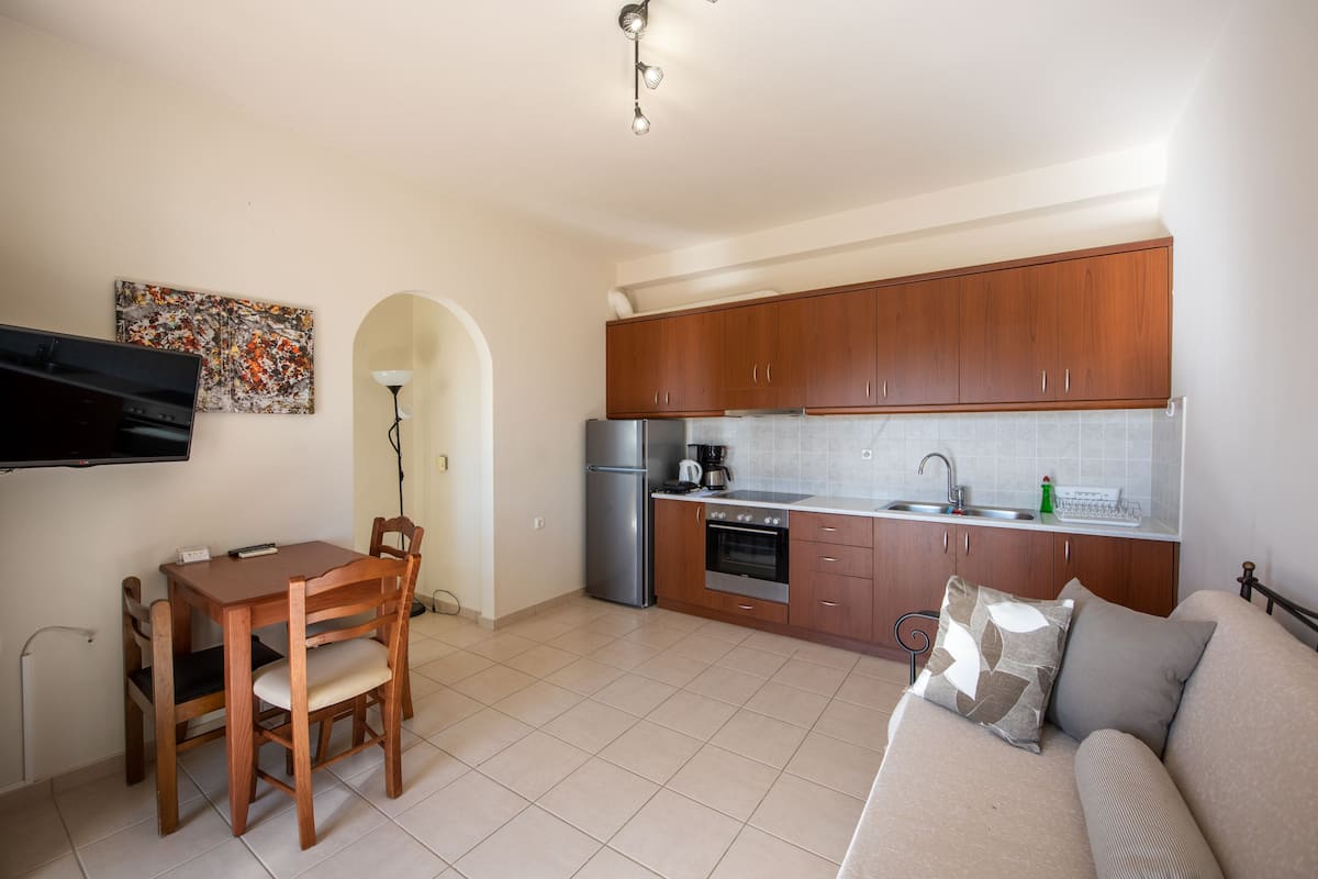 A compact kitchen with wooden cabinets, a refrigerator, an oven, and a dining table with chairs.