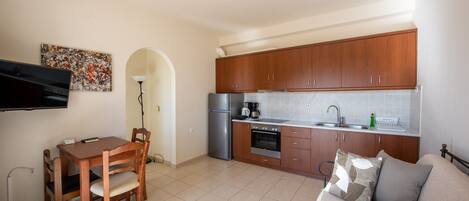 Una cocina compacta con armarios de madera, un refrigerador, un horno y una mesa de comedor con sillas.