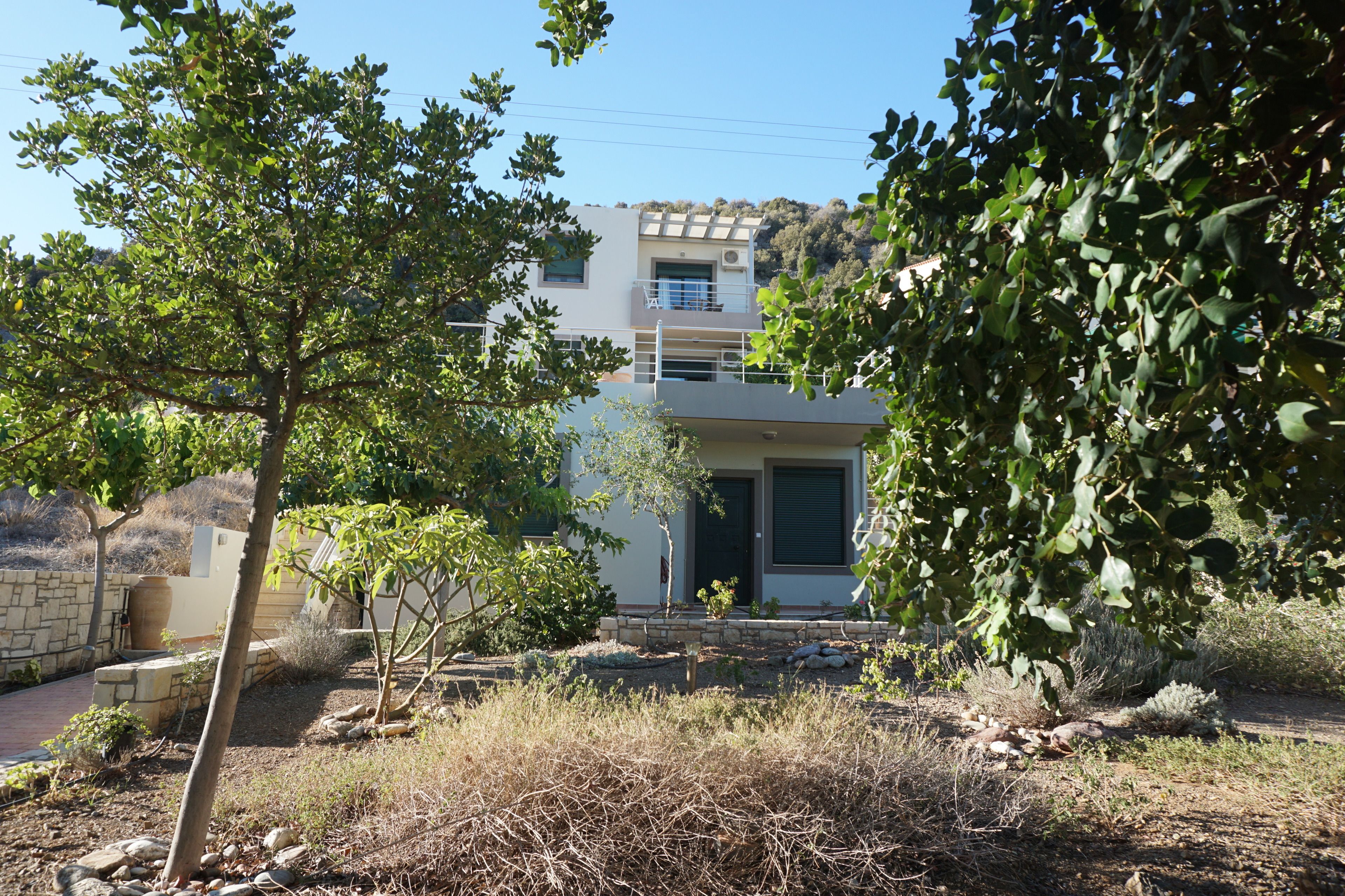 Ein modernes, zweistöckiges Haus mit einer Steinwand, einem kleinen Garten und Blick auf eine Hügelterrasse.
