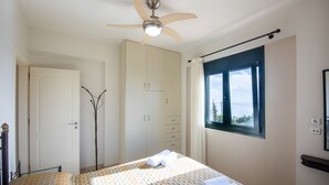 Un dormitorio con cama, ventilador de techo, armario, ventana con vistas y puerta.