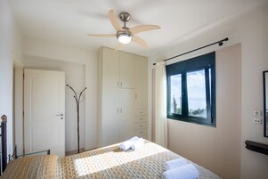 Un dormitorio con cama, ventilador de techo, armario, ventana con vistas y puerta.