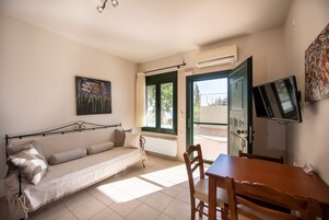 Una habitación con sofá, mesa de comedor, televisor y ventana con cortinas.