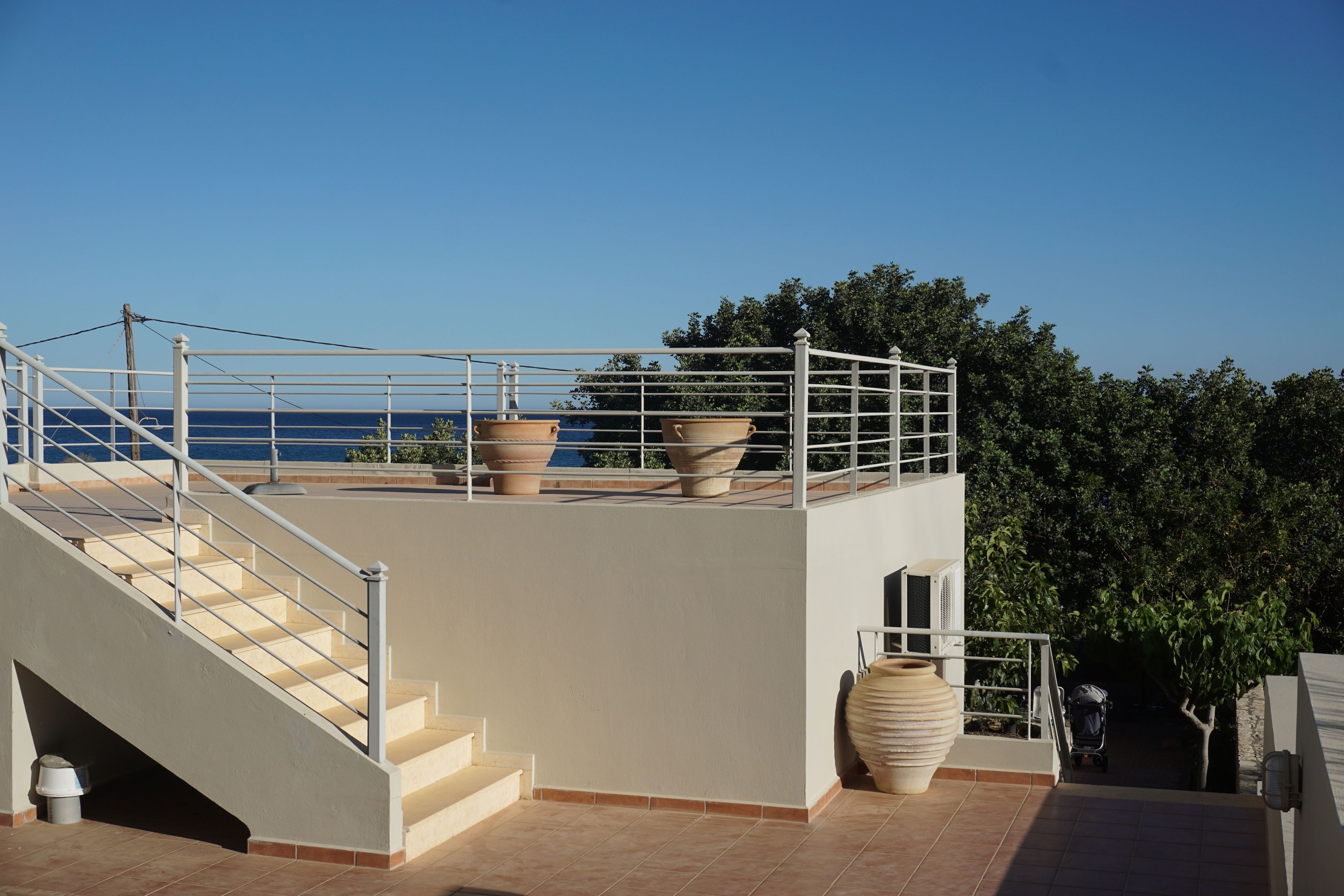 A rooftop terrace with a staircase, outdoor seating area, and large planters.
