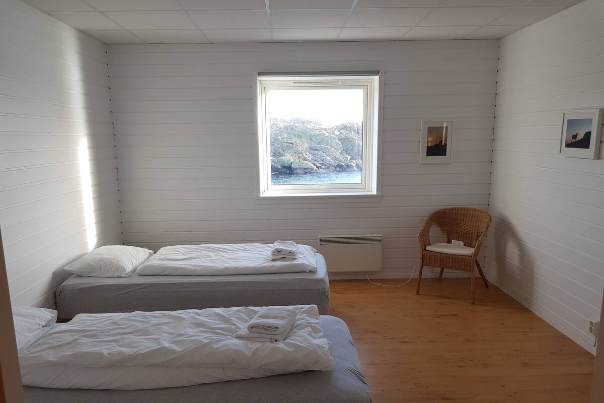 Una habitación con dos camas, una ventana con vistas a las montañas, una silla de mimbre y un radiador.