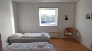 Quarto com duas camas, janela com vista para montanhas, cadeira de vime e radiador.