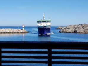 Un barco grande amarrado en un puerto, con un faro y afloramientos rocosos al fondo.