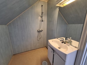 Un baño con ducha, lavamanos y armario.