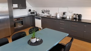 Uma cozinha moderna com eletrodomésticos de aço inoxidável, uma área de jantar com mesa e cadeiras, e uma planta em vaso sobre a mesa.