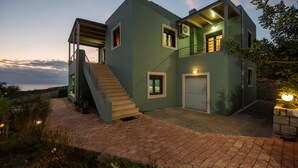 A modern two-story house with a staircase leading to the upper level, a garage, and a brick pathway. - Portela Villas Kapsali (Viannos)