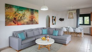 A modern living room with a grey sectional sofa, a round coffee table, and a large abstract painting on the wall. - Portela Villas Kapsali (Viannos)