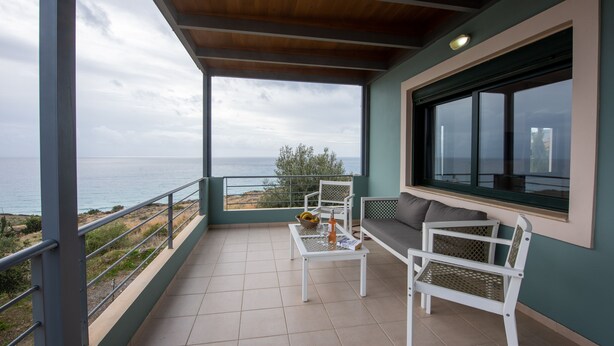 A balcony with a view of the sea, a table with a basket, and two white chairs. - Portela Villas Kapsali (Viannos)