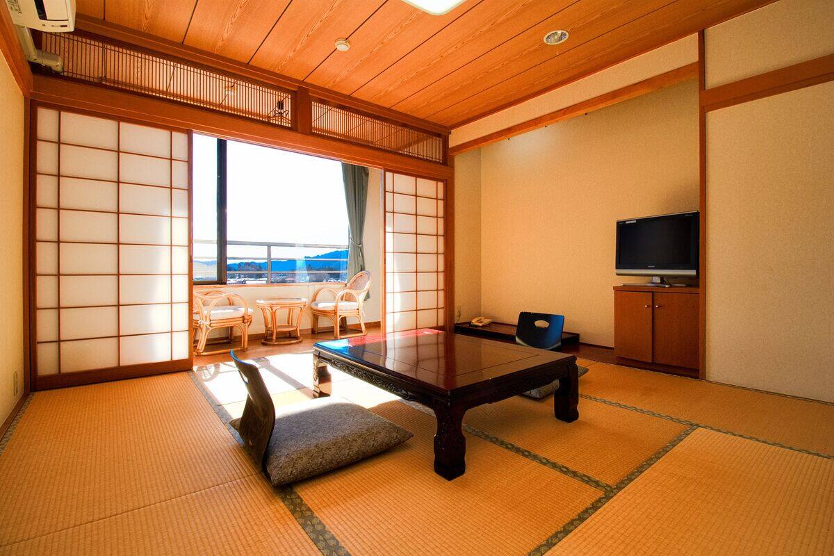 Ein traditioneller japanischer Raum mit Tatami-Böden, einem niedrigen Tisch, einem Fernseher und Blick ins Freie.