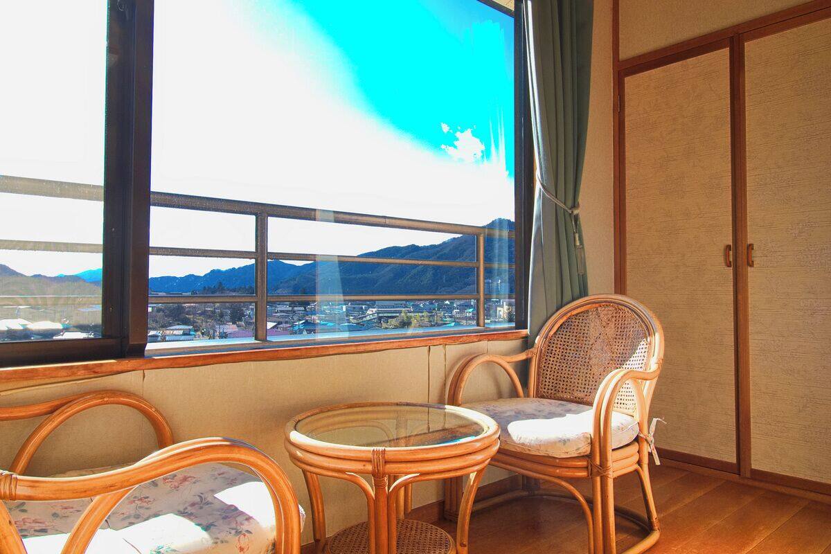 Ein Zimmer mit großem Fenster, Korbsesseln, einem kleinen Tisch und einer Schiebetür.