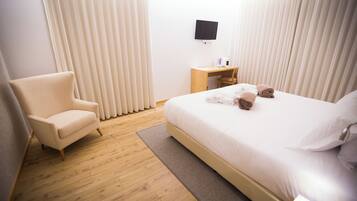 Una habitación de hotel con cama, una silla, un escritorio y televisión en la pared.