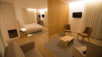 Una habitación de hotel moderna con cama, sofá, sillón y televisor en la pared.