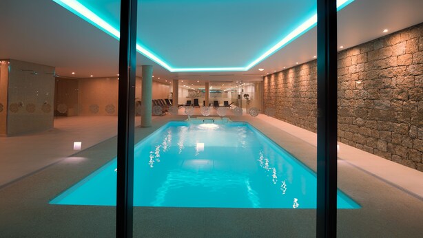 A modern indoor swimming pool with a stone wall and recessed lighting. - Lam Hotel Celorico de Basto (Celorico de Basto)