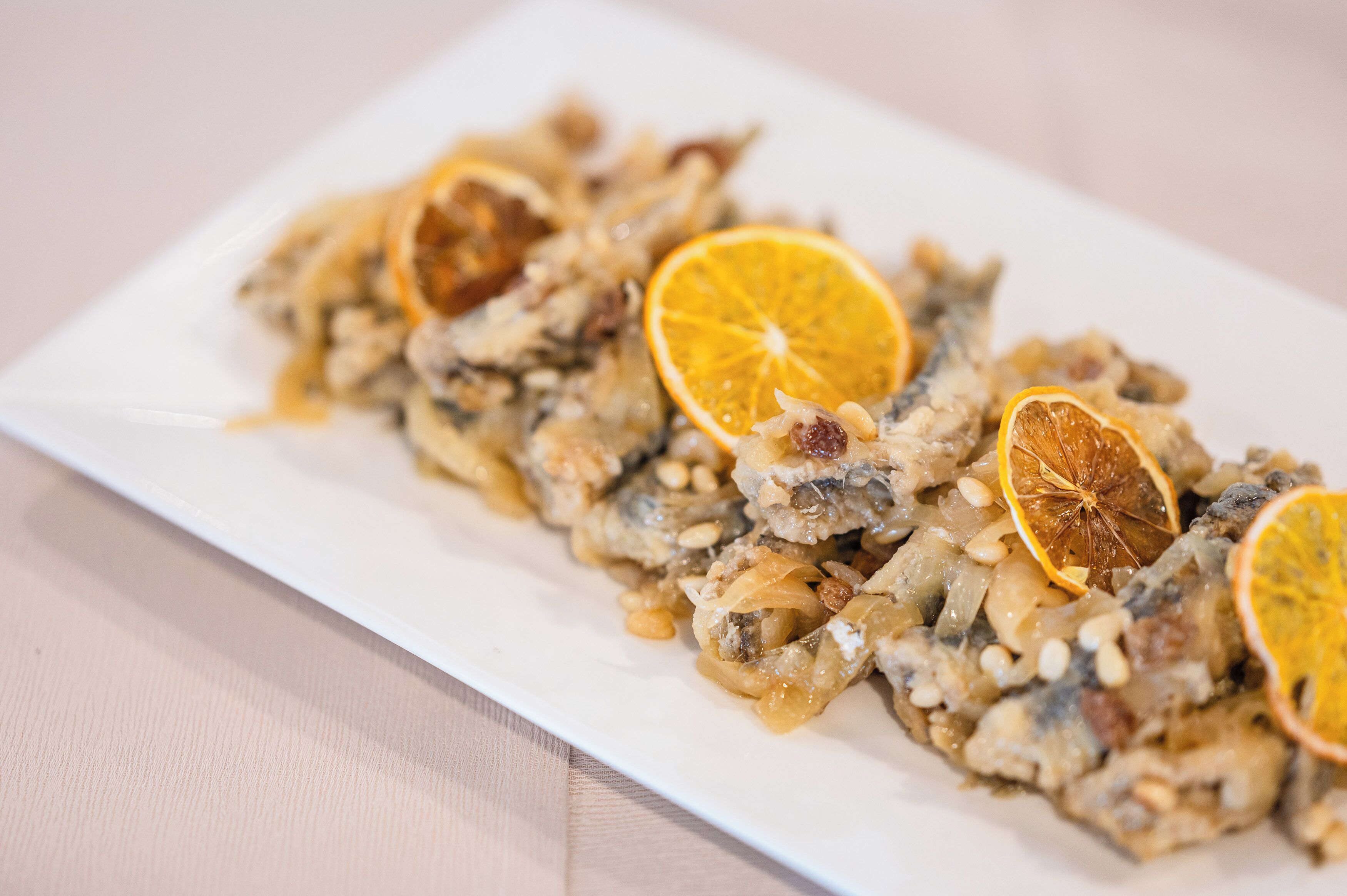 Un plato rectangular blanco con un guiso adornado con rodajas de naranja deshidratada.