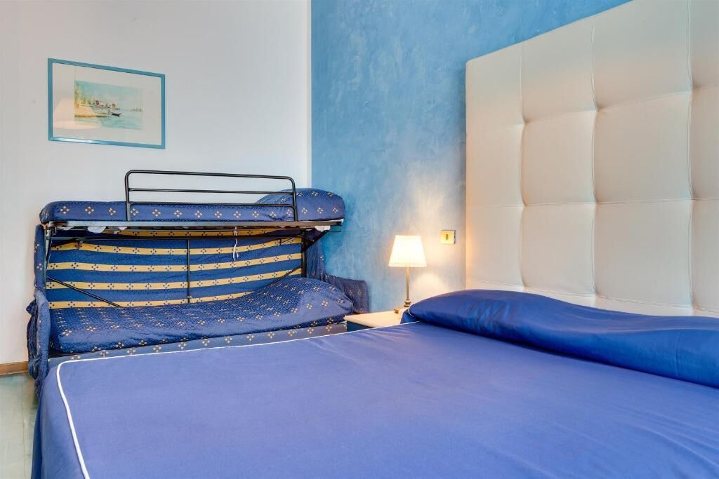 Un dormitorio con una cama litera, una cama individual, una lámpara de noche y un cuadro en la pared.