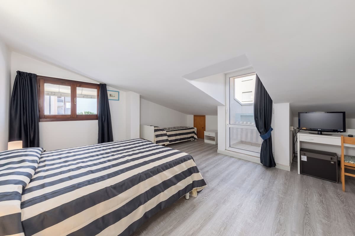 A bedroom with a large bed, a desk, a television, and a window with curtains.