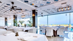 A restaurant with white tablecloths, wicker chairs, and a view of the ocean. - Hotel Gritti (Jesolo)