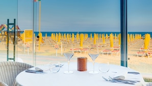 A table set for dining with a view of a beach with yellow umbrellas. - Hotel Gritti (Jesolo)
