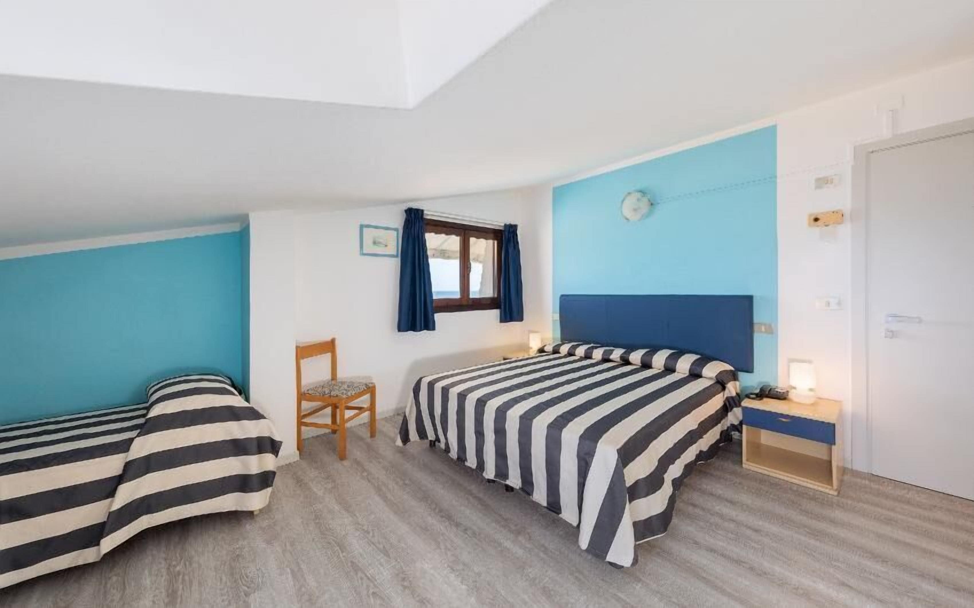 A room with two beds, a chair, a desk, a window with curtains, and a clock on the wall.