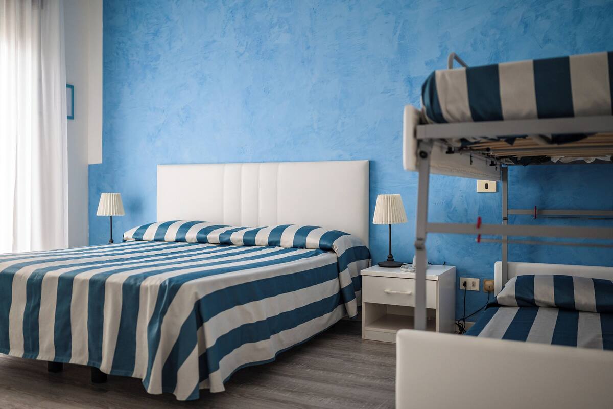 A hotel room with a bunk bed, a single bed, and a bedside table with a lamp.