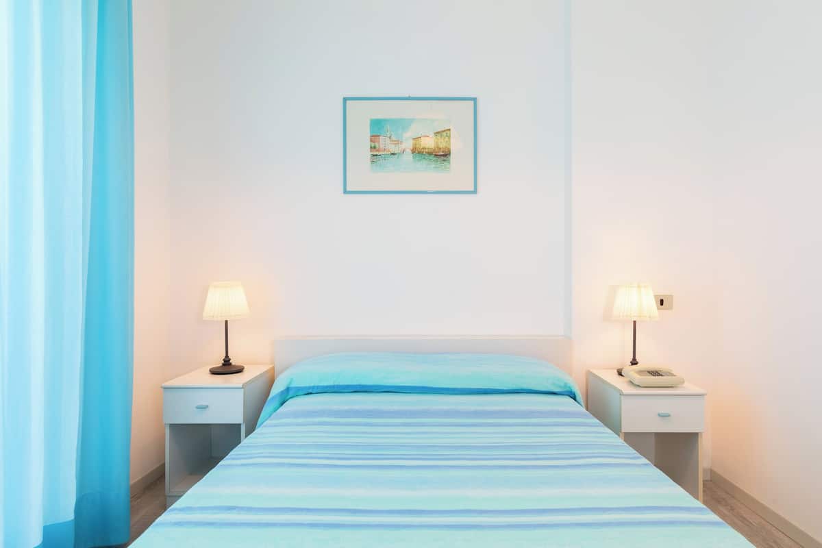 A hotel room with a bed, two bedside tables with lamps, a framed picture on the wall, and a blue curtain.