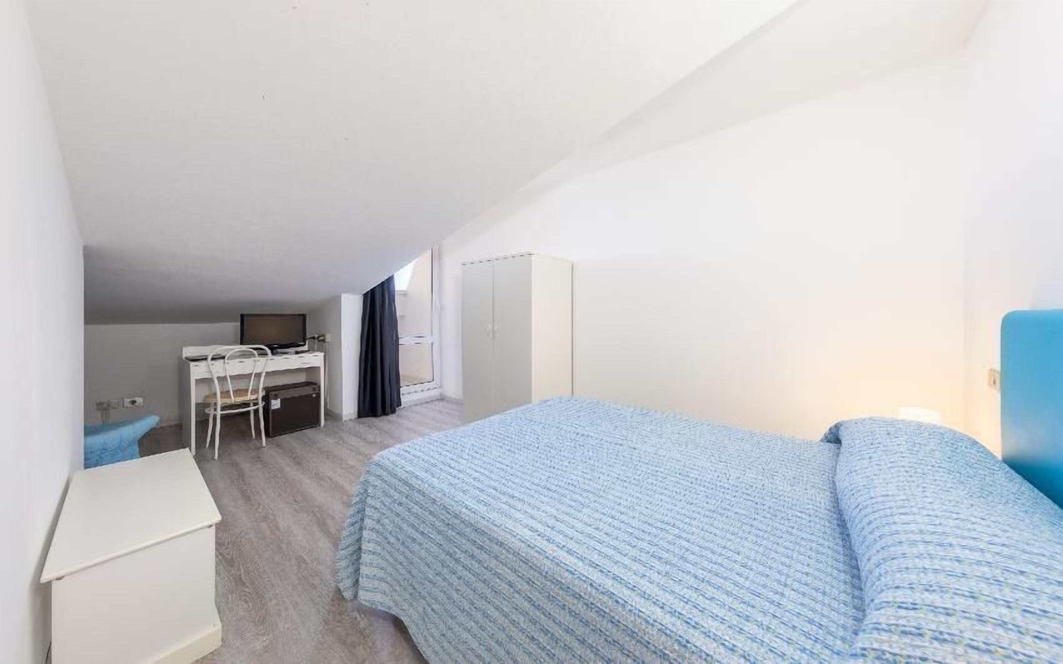 A compact room with a bed, a desk, and a wardrobe.