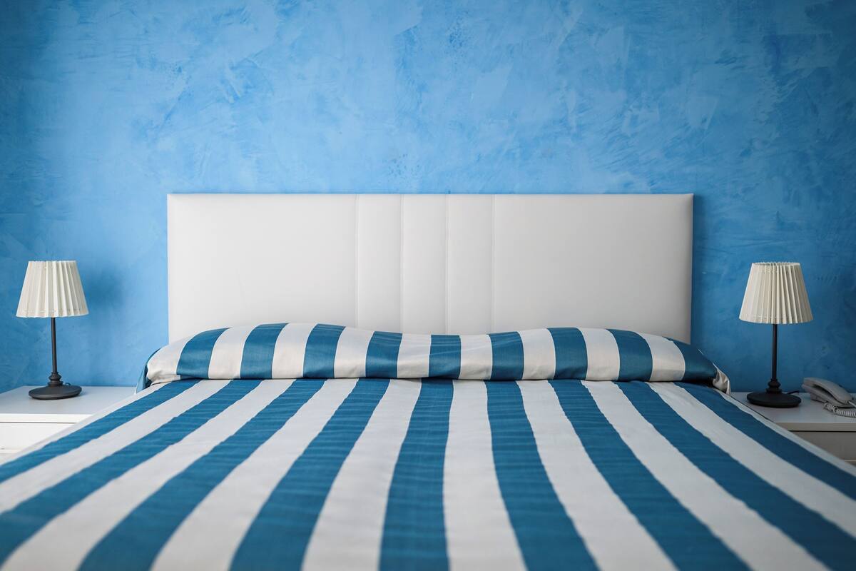 A bed with a white headboard and blue-striped bedding, two bedside lamps, and a white telephone on a nightstand.