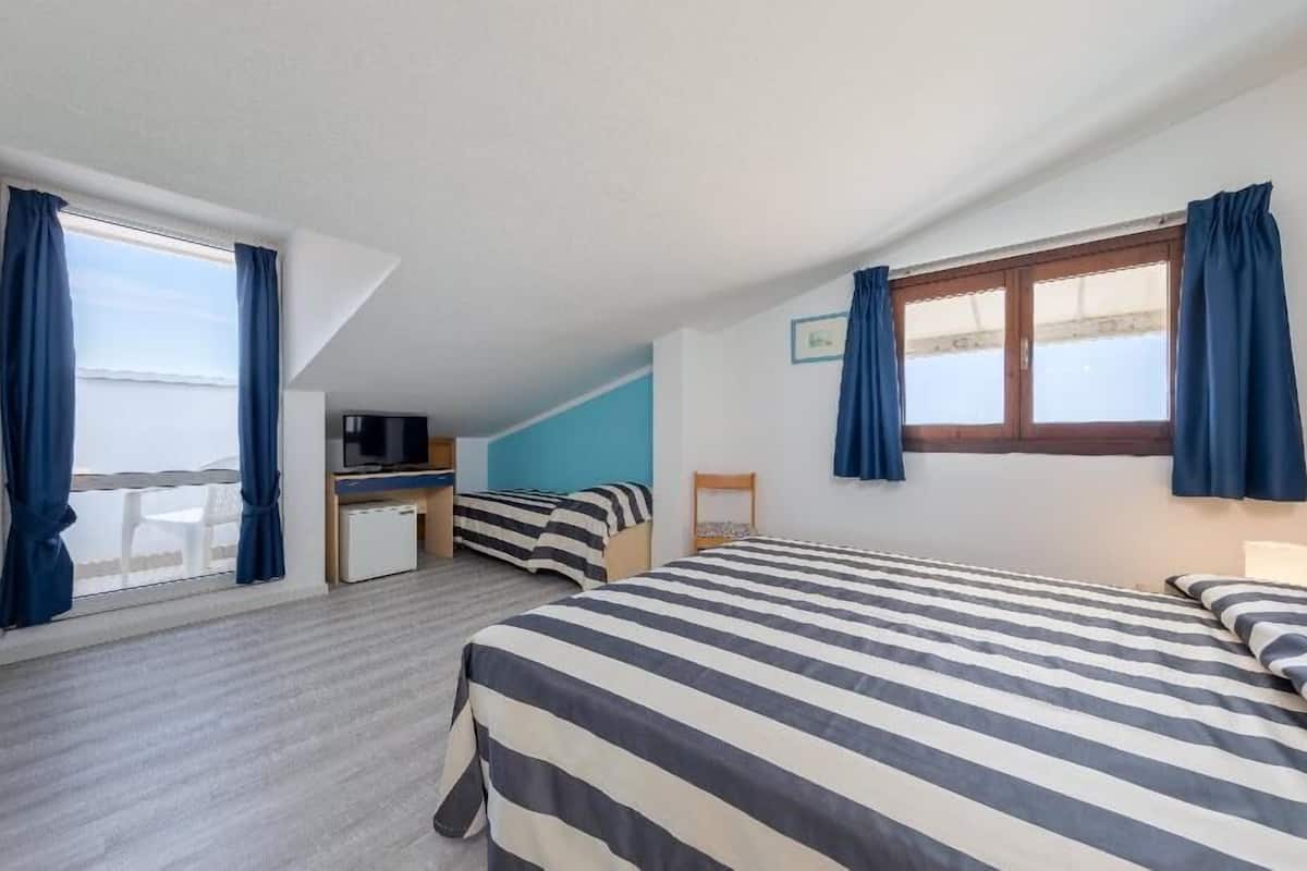A bedroom with two beds, a desk with a TV, and a window with curtains.