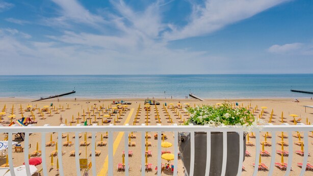 A beach with rows of sunbeds and umbrellas, a pier extending into the water, and a clear blue sky. - Hotel Gritti (Jesolo)