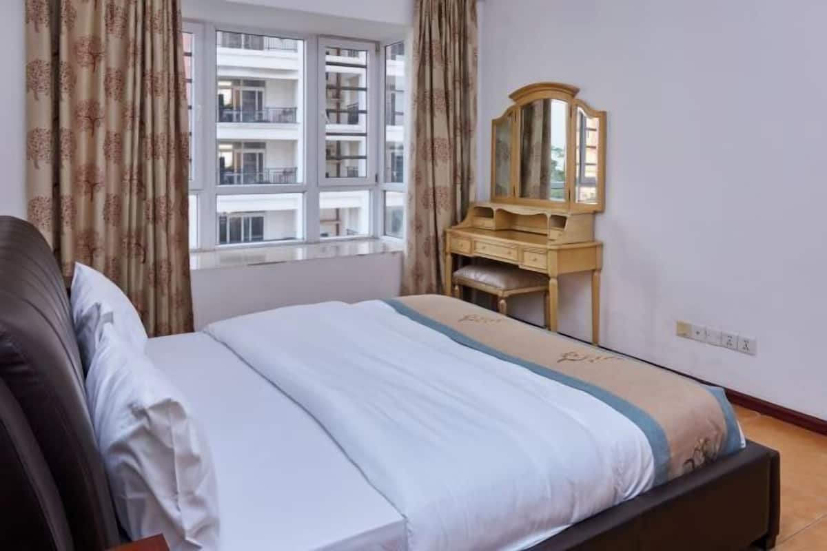 Une chambre à coucher avec un lit, une commode, un miroir et une fenêtre avec des rideaux.