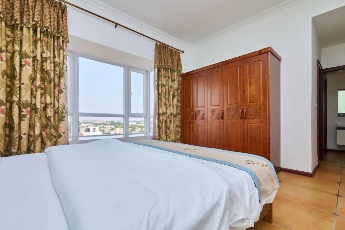 Une chambre à coucher avec un lit, une armoire, une fenêtre avec des rideaux et une vue sur l’extérieur.