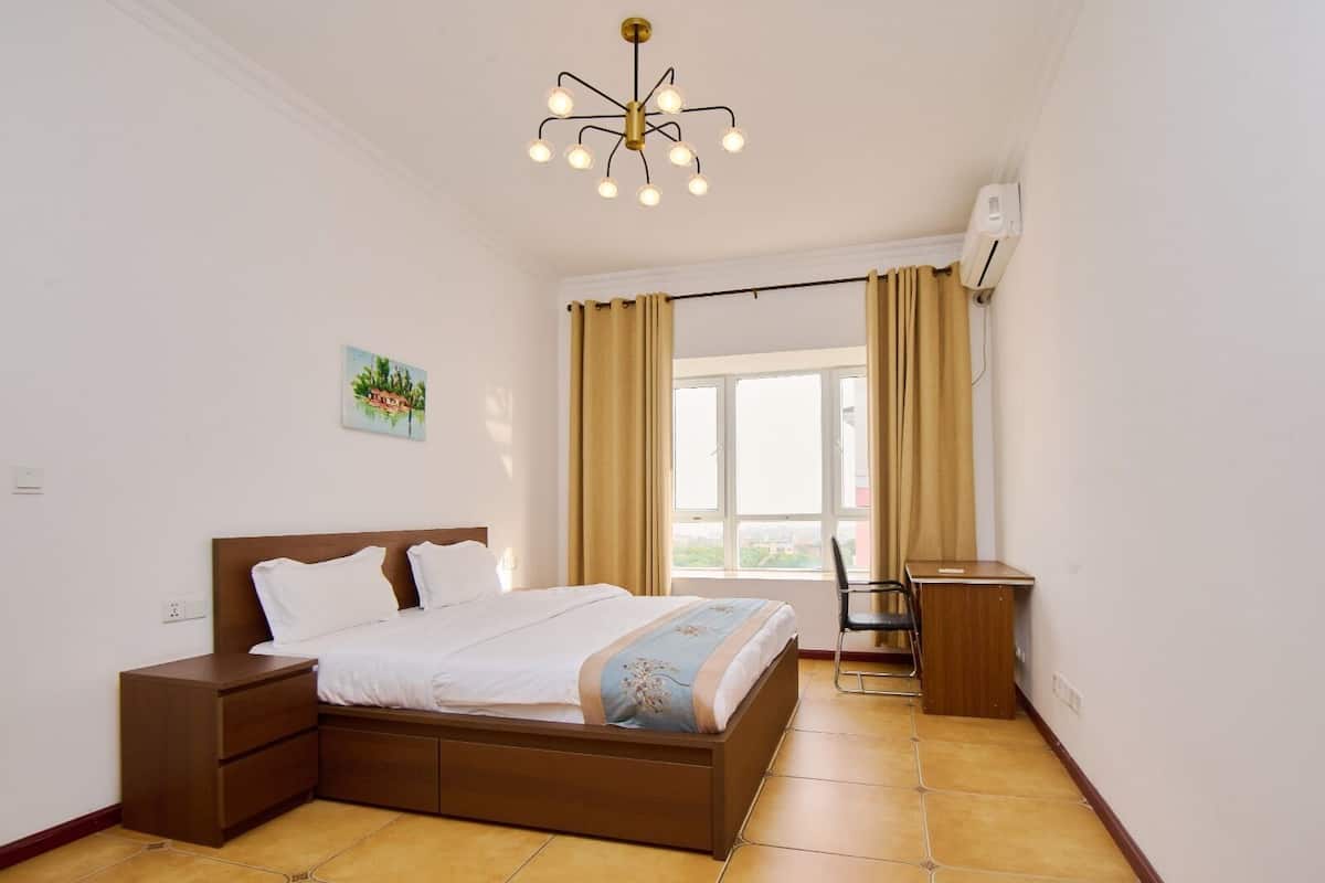 Une chambre à coucher avec un lit, des tables de chevet, un bureau et une fenêtre avec des rideaux.