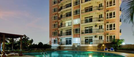 Un hotel de varios pisos con piscina, balcones y mobiliario exterior.